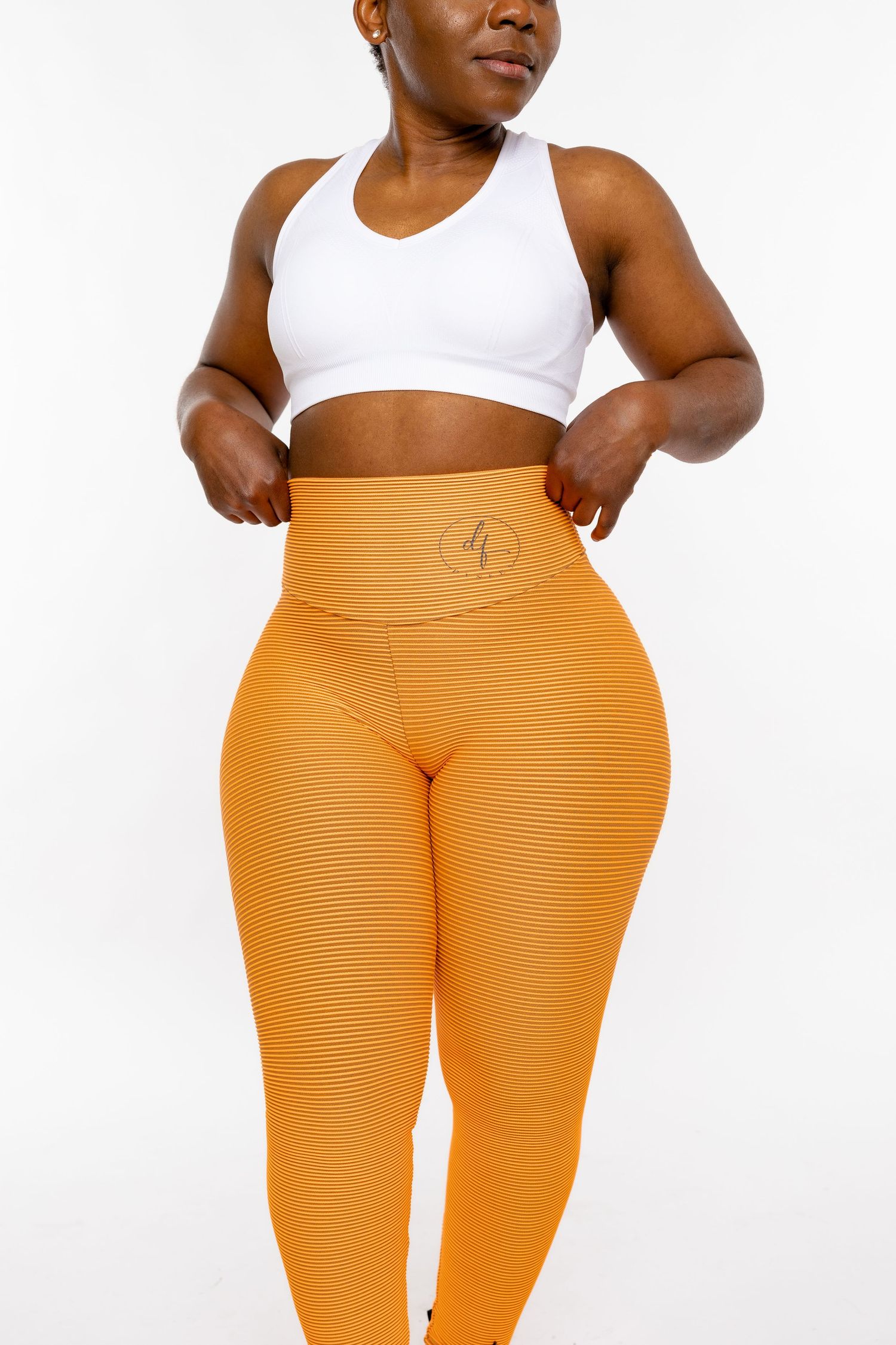 Woman wearing orange ribbed high-waist leggings and white sports bra, showcasing athletic activewear set.