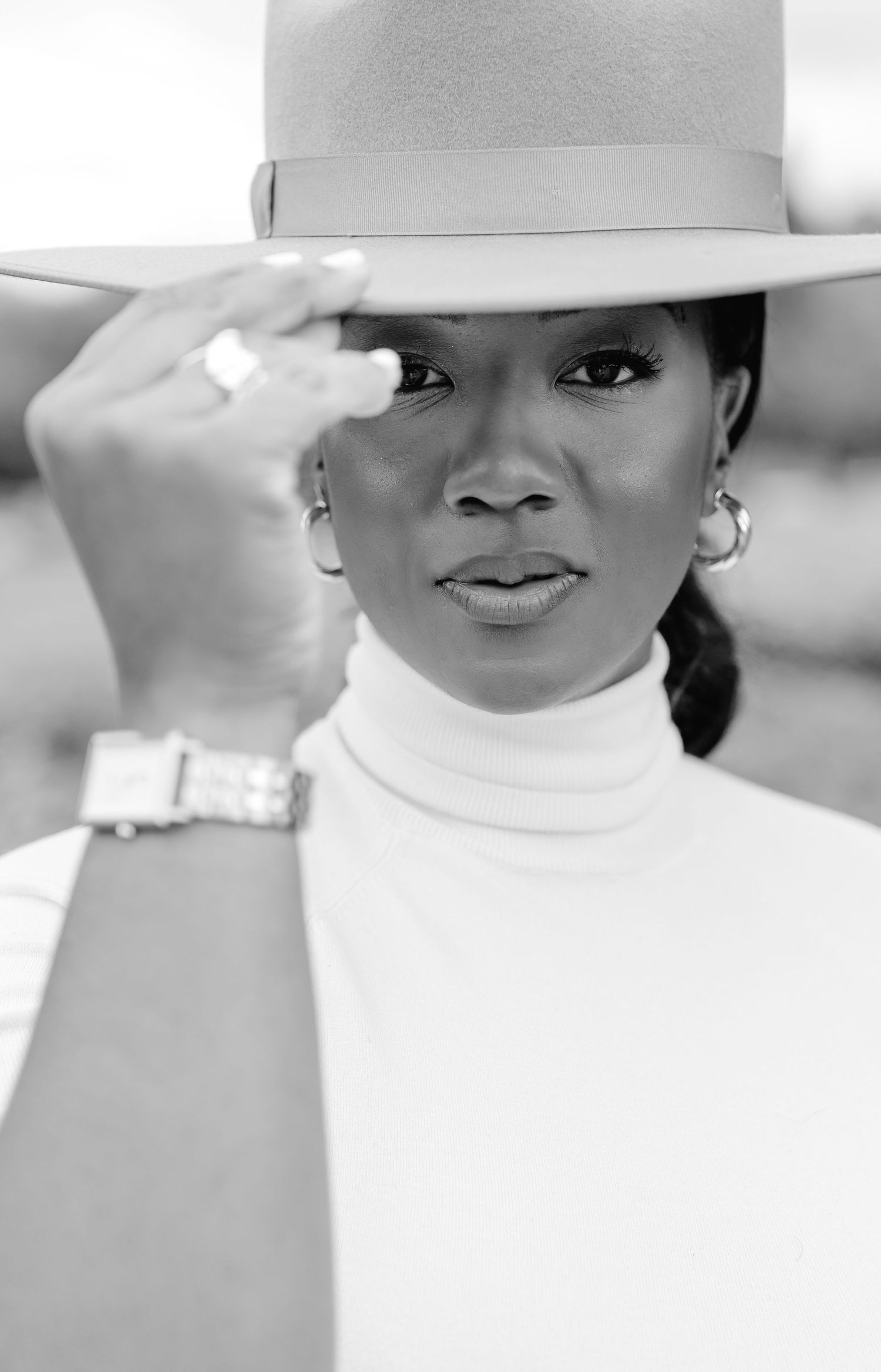 Black and white fashion portrait of someone wearing a white turtleneck and gray fedora hat with a wristwatch.