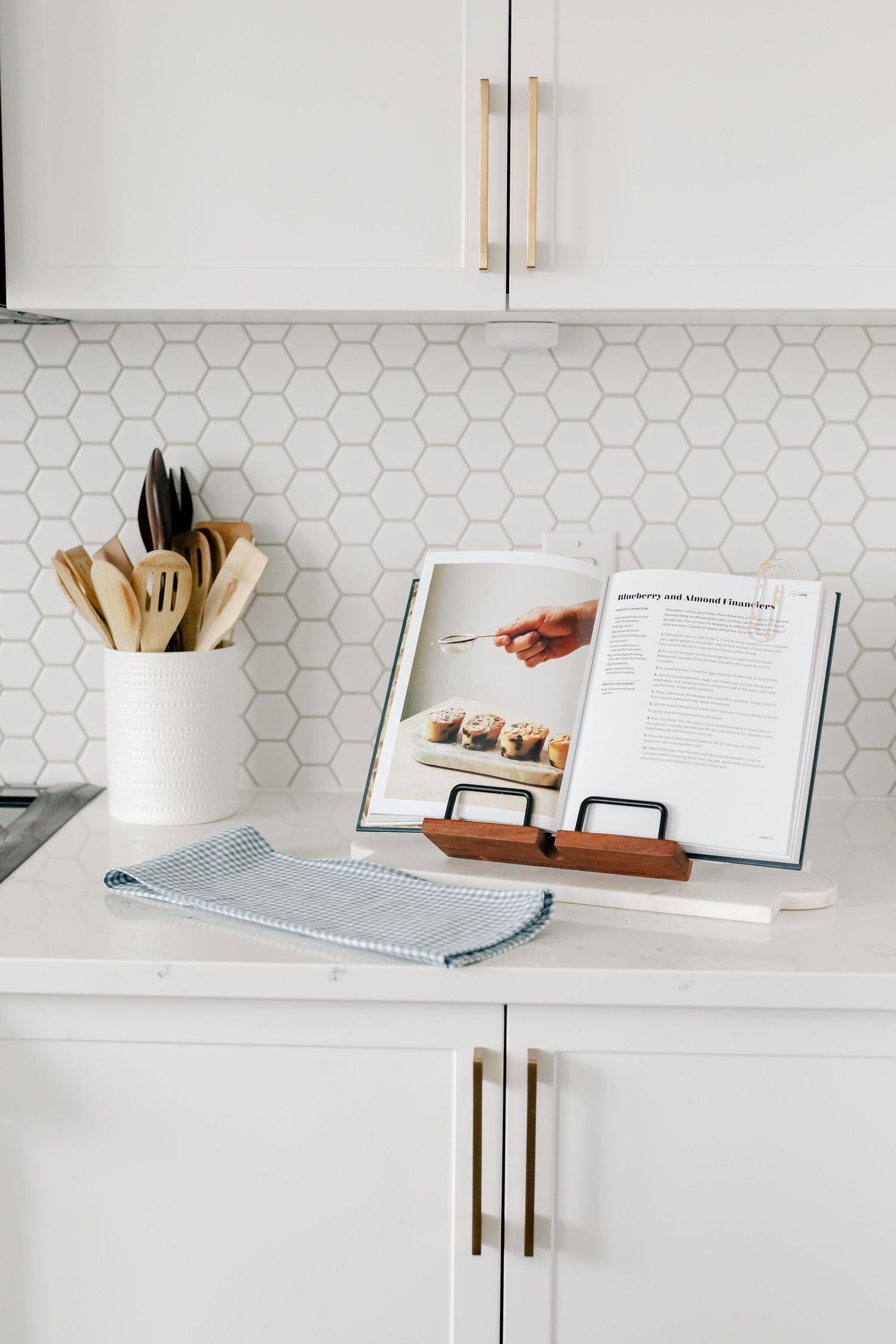 Minimalist white kitchen counter with cookbook, utensils, and hexagonal tile backsplash shown in progression.