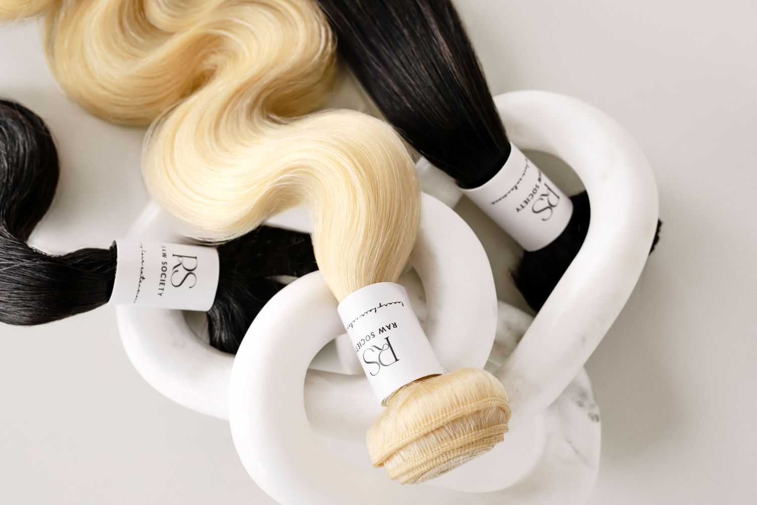 Bundles of black and blonde hair extensions displayed on white curved holders with numbered labels.