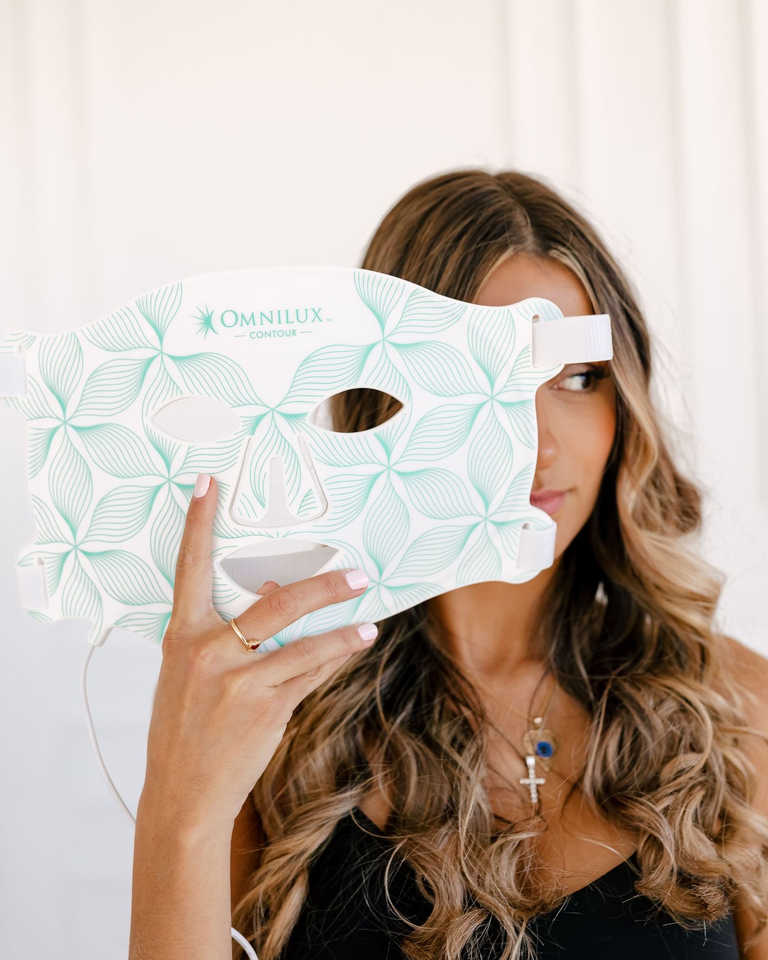 Someone holding up a blue and white patterned Omnilux LED light therapy face mask against a white background.