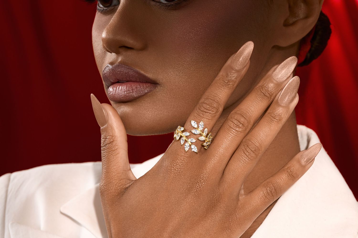 Woman wearing an elegant gold floral ring with white stones, styled with nude nails and a white blazer.