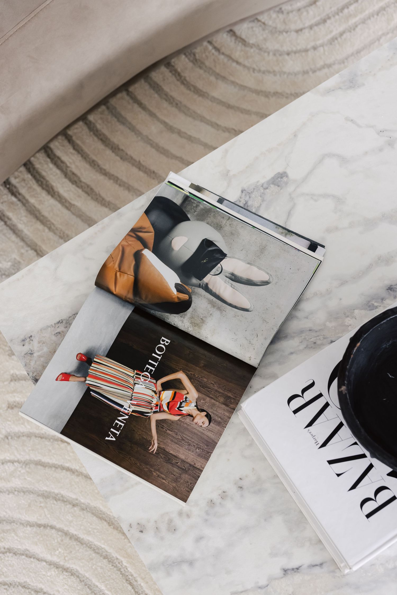 Marble coffee table with Bottega Veneta book and Harper's Bazaar magazine, styled in a luxurious living room.
