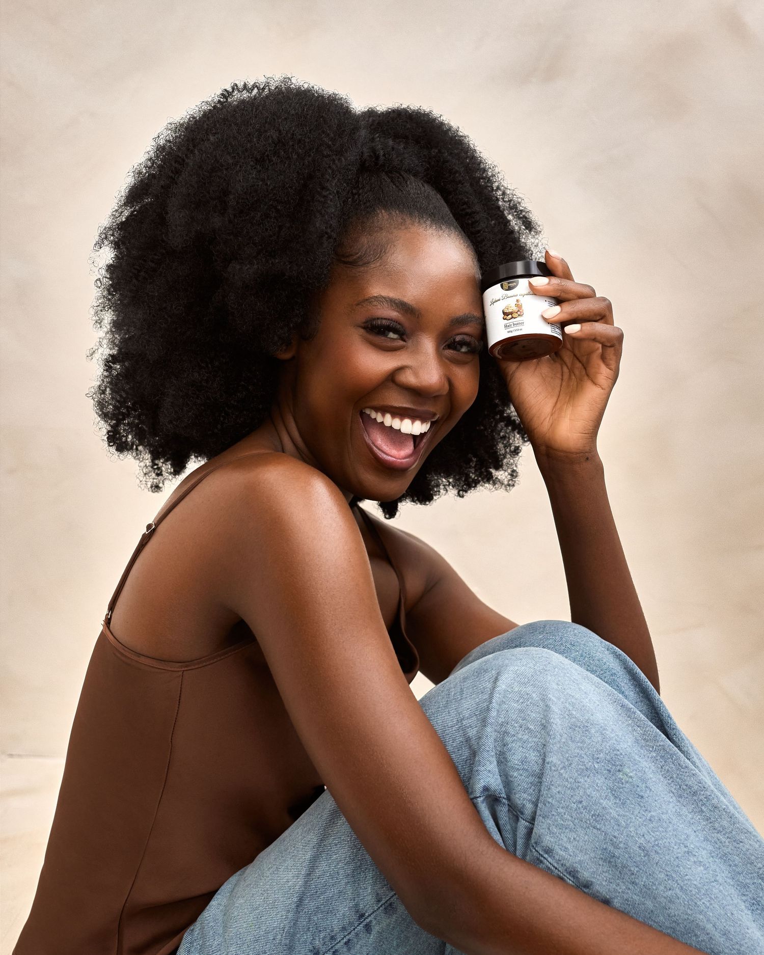 A woman in a brown sleeveless top and jeans lounges comfortably while holding a coffee mug and smiling.