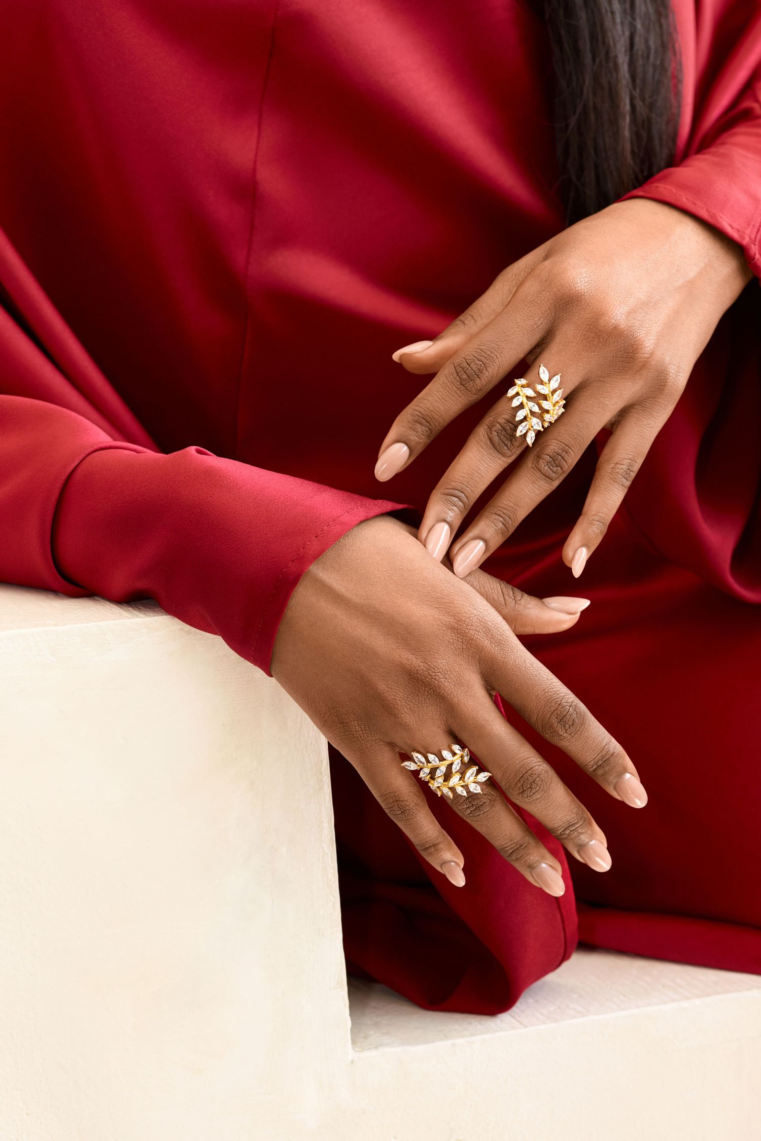 Close up of hands wearing delicate gold leaf rings against red silk fabric.