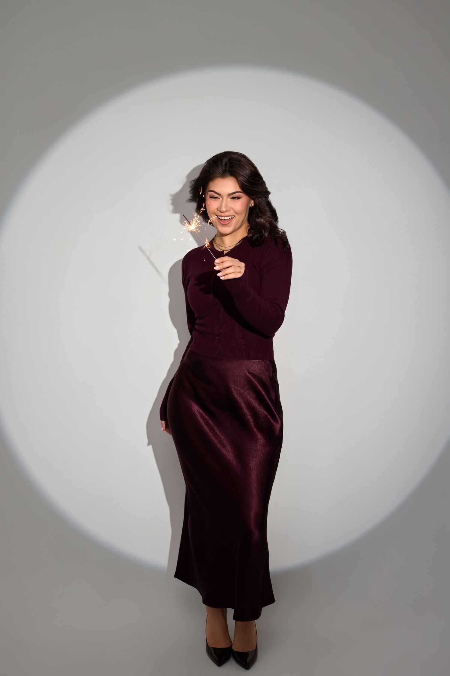 Person in a burgundy sweater dress poses playfully against a grey studio backdrop in a series of candid shots.