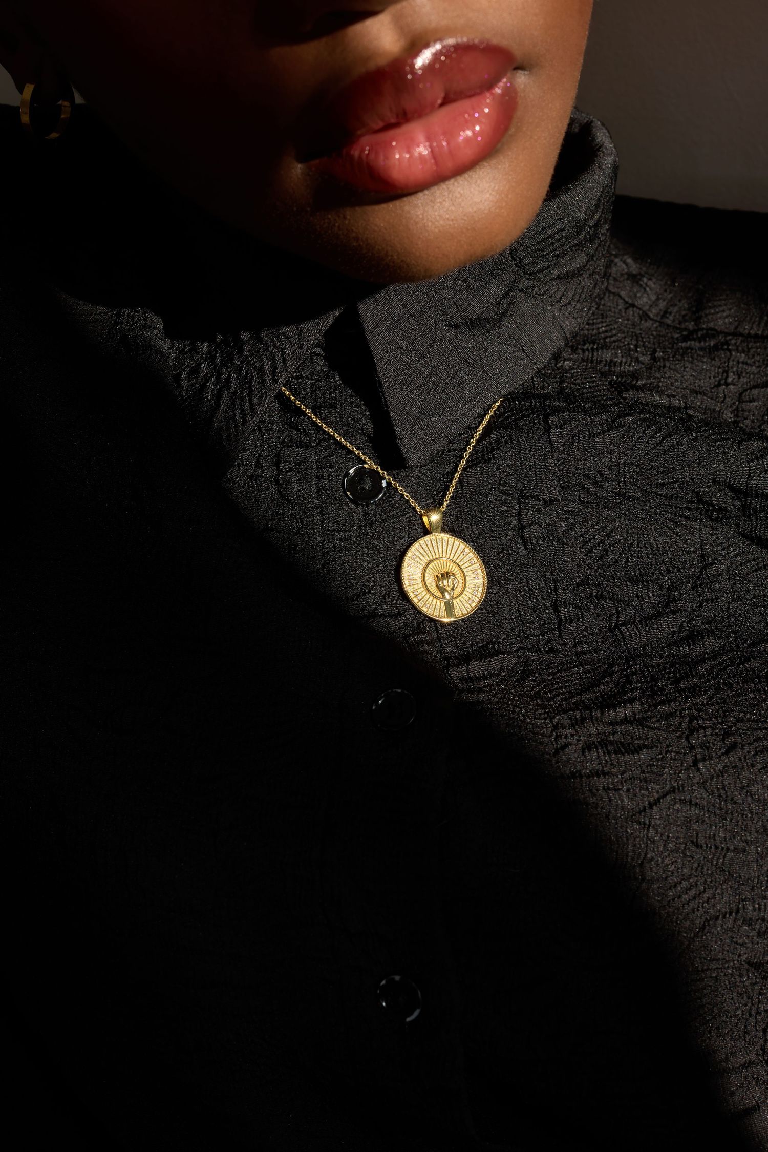 Gold coin pendant necklace with portrait detail on a model wearing a black textured turtleneck jacket.