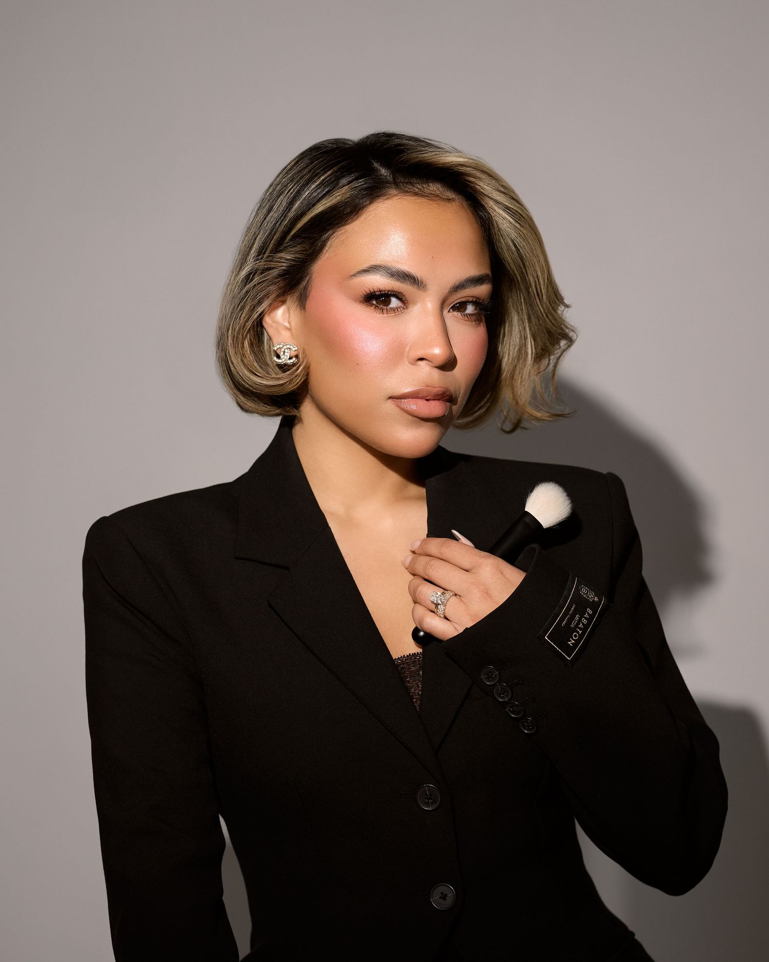 A person poses in a black blazer against a neutral background in a series of editorial style photos.