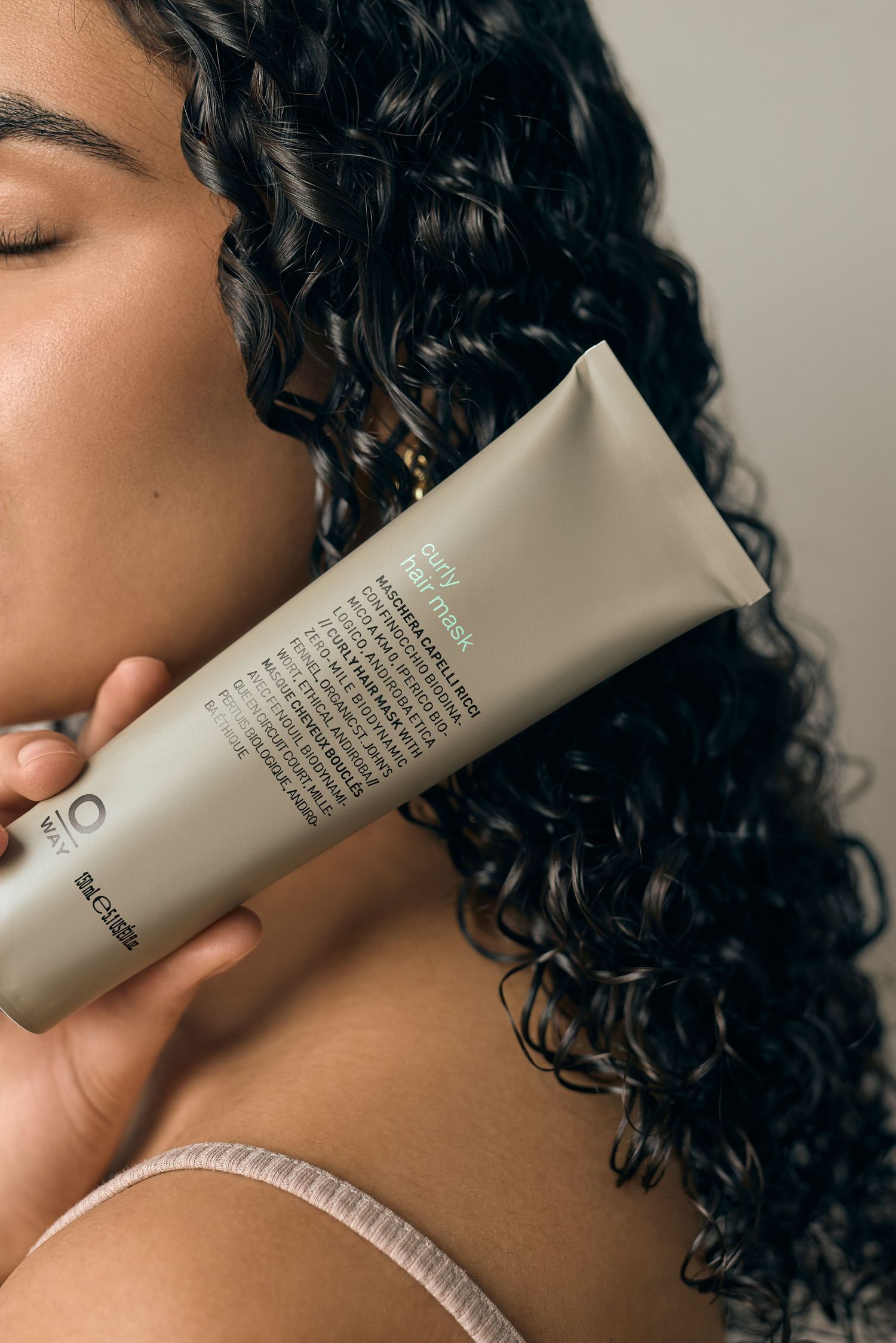 Close up of curly hair with beauty product tube against neutral background.