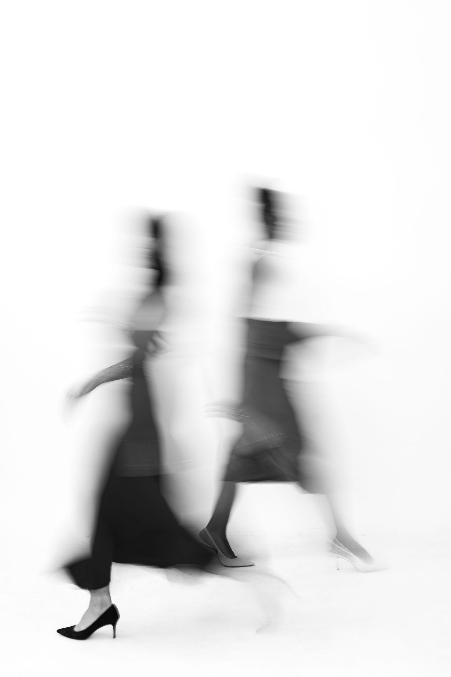 Blurred motion silhouettes of people dancing in black and white against a white background.