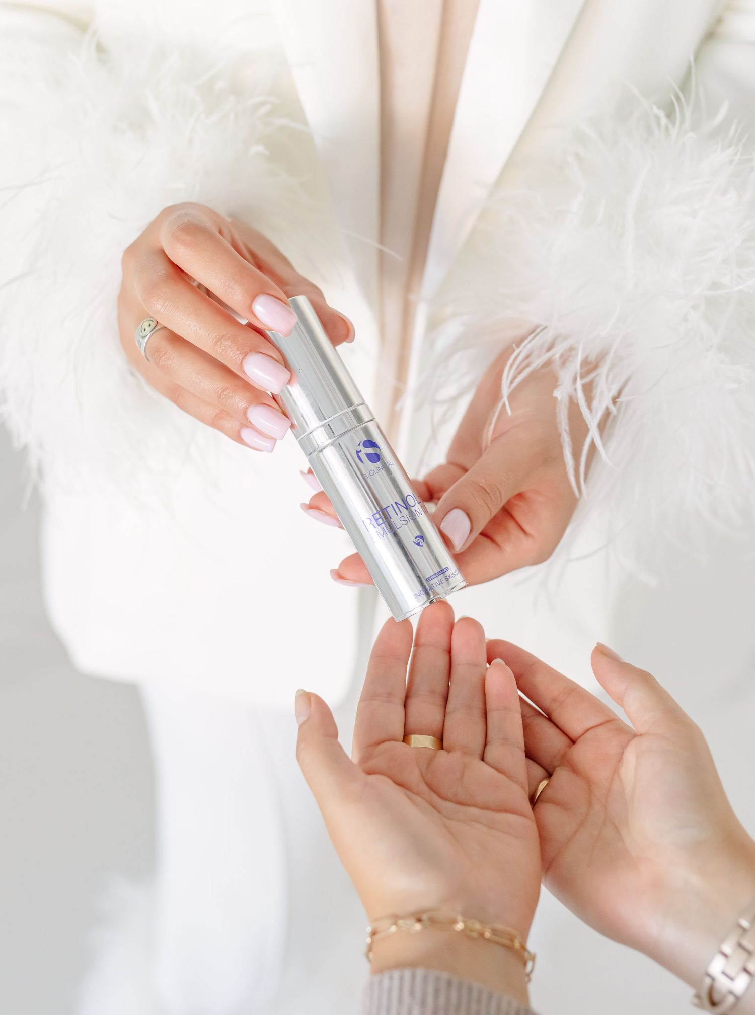 Hands holding and applying A face serum product against white fluffy fabric background.
