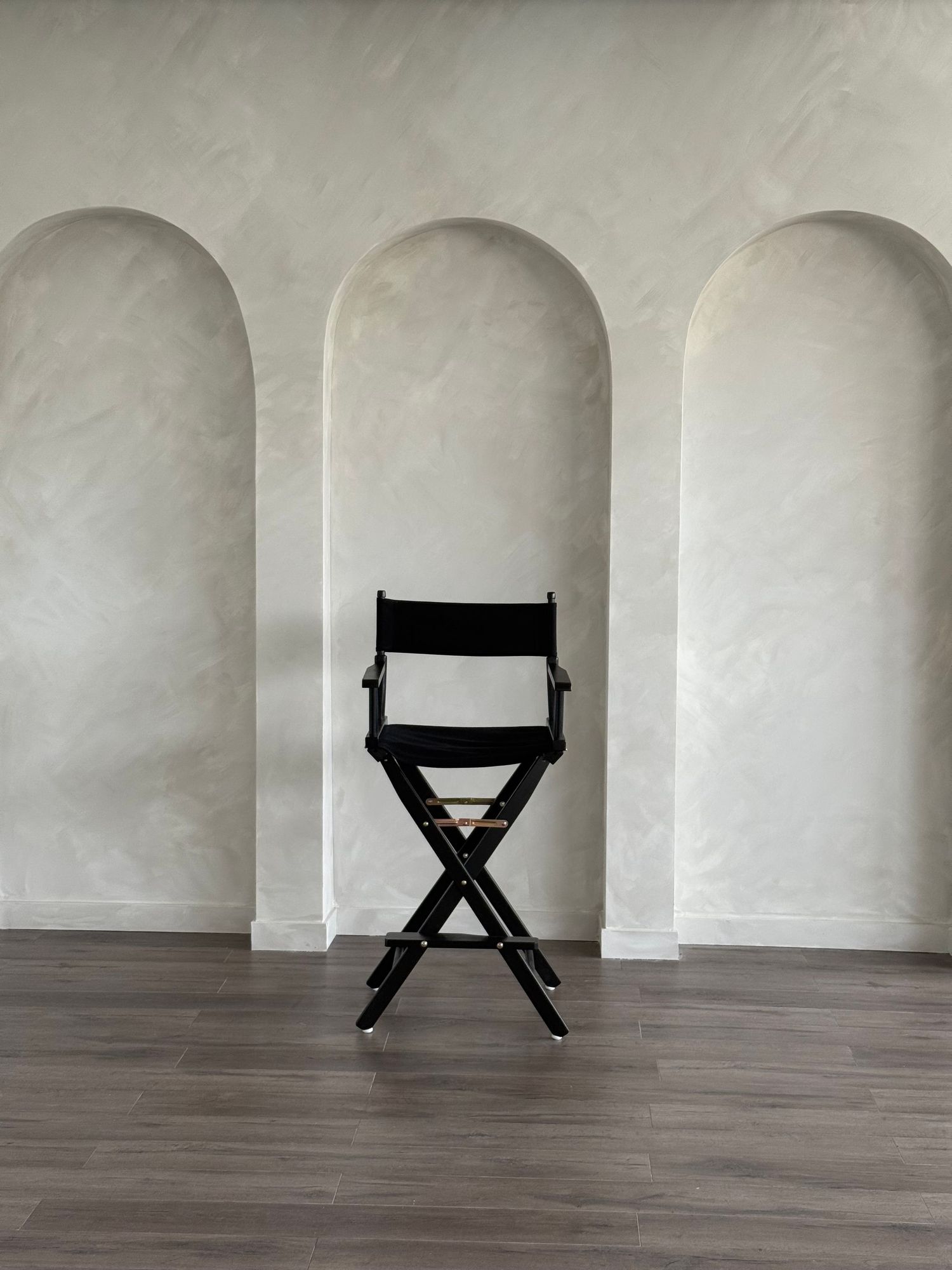 Black director's chair centered between three white arched alcoves on wooden floor.