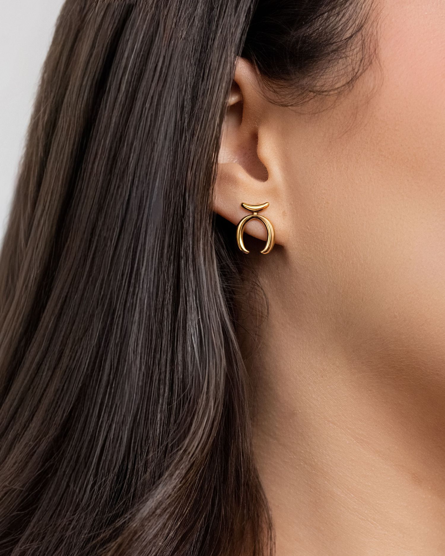 Gold crescent moon stud earring worn by a dark-haired model, showcasing elegant minimalist jewelry design.