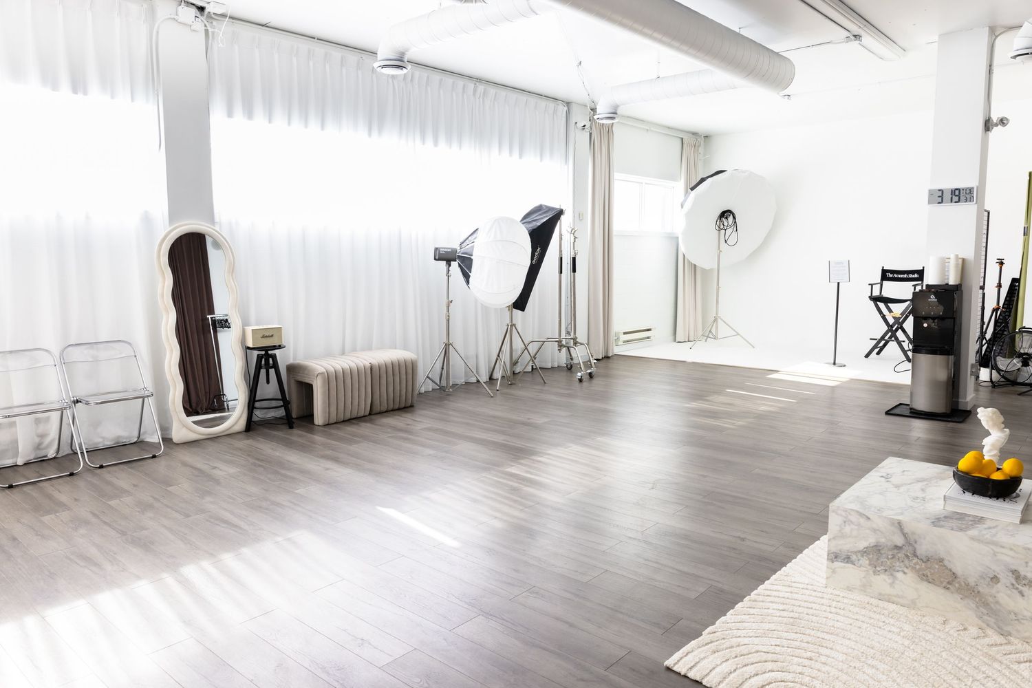 Bright photography studio with hardwood floors, professional lighting equipment, large windows, and minimalist white decor.