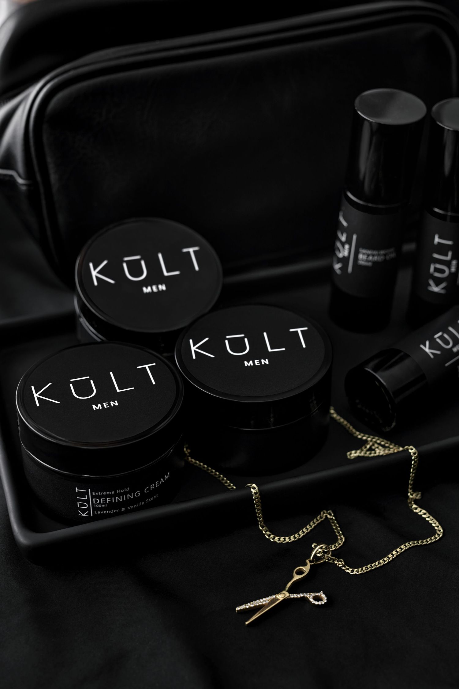 Black Kuli skincare product jars with gold chain accessories displayed against dark background.