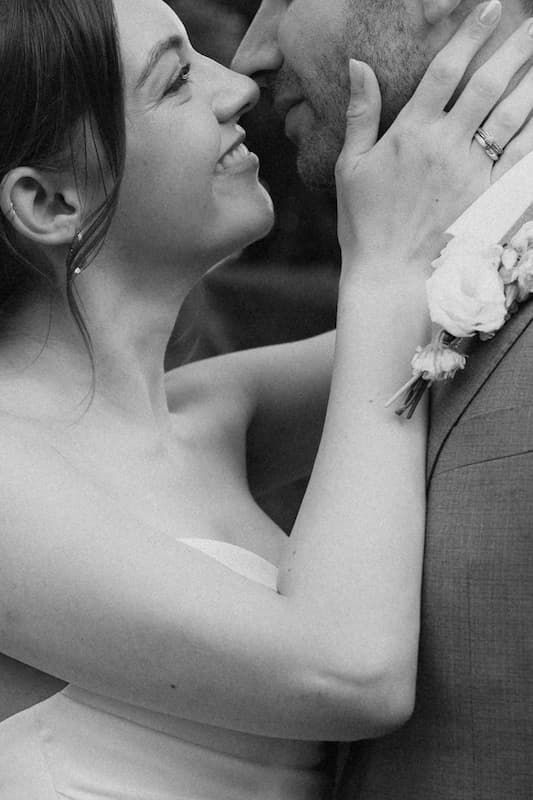 Black and white wedding photo of smiling bride gazing up at groom, her hand on his chest showing a ring.