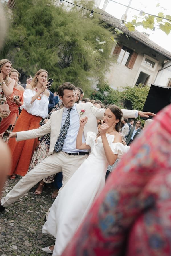 Bride and groom dancing joyfully outdoors at wedding reception surrounded by cheering guests.