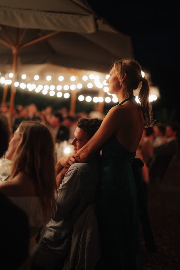 Couple embracing at an outdoor evening wedding reception with string lights glowing in the background.