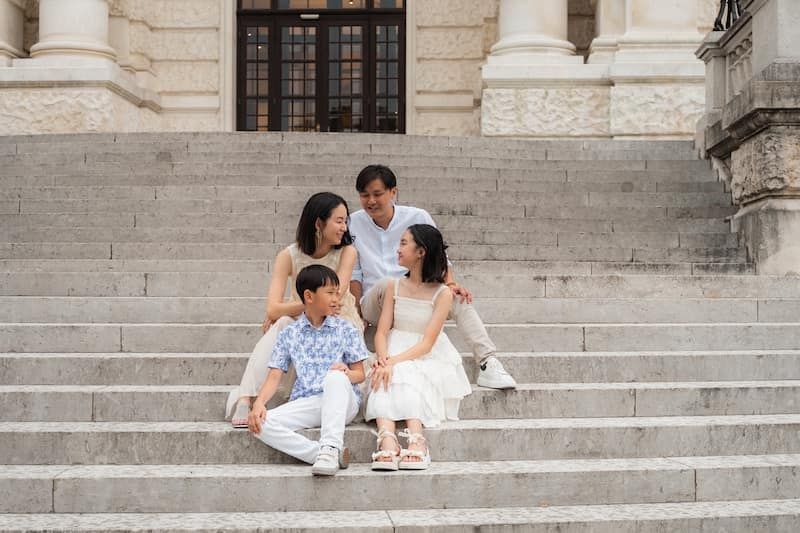 Die 4-köpfige Familie sitzt auf den Stufen der Hofburg und reden lachend miteinander