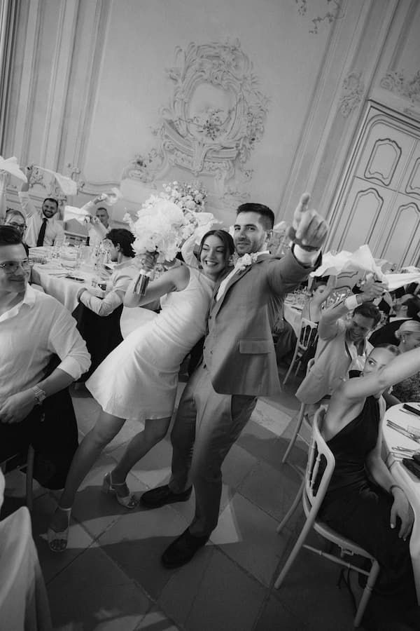 Black and white photo of a joyful couple dancing at a wedding reception in an elegant ballroom.