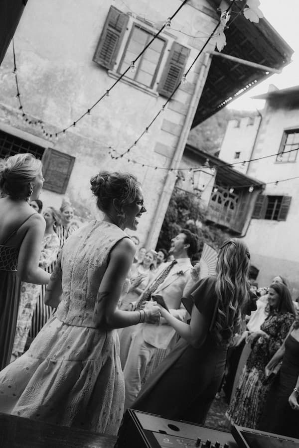 Black and white photo of guests dancing outdoors at a rustic European wedding reception with string lights.