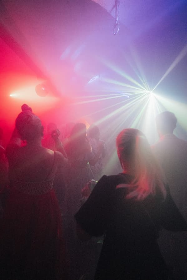 People dancing in a nightclub with colorful pink and blue laser lights illuminating the dance floor.