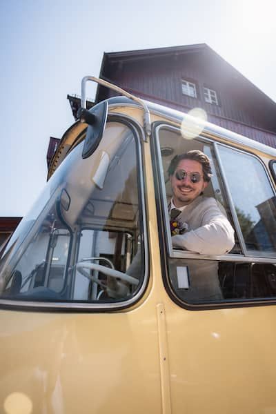 Der Bräutigam sieht aus dem Seitenfenster des Oldtimerbusses.