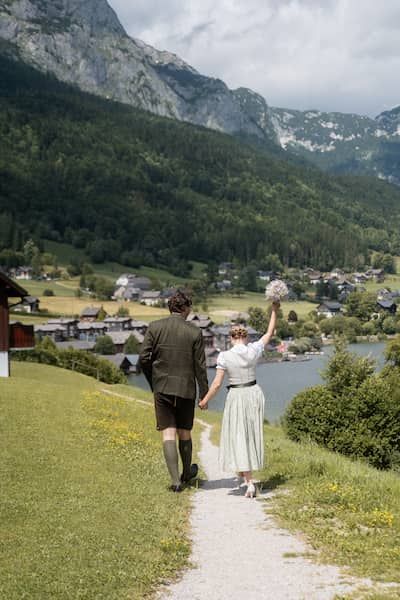 Braut & Bräutigam in Tracht. Die Braut streckt ihren Arm mit dem Brautstrauß nach oben.