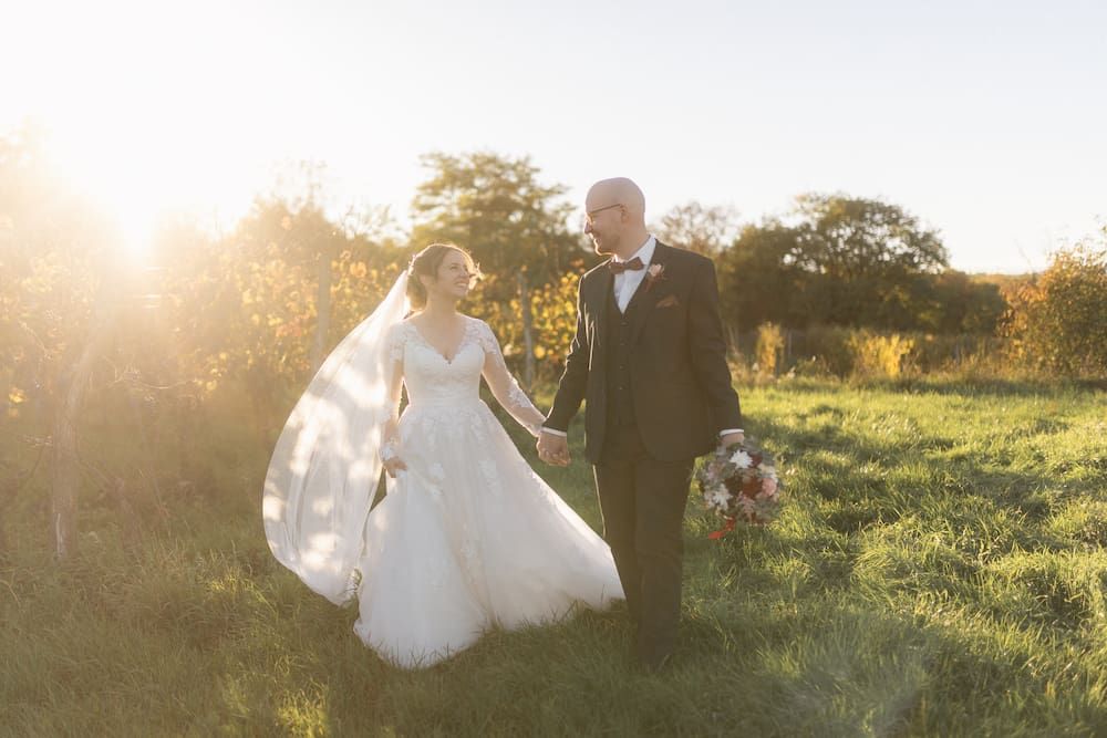 Katrin & Christoph gehen Hand in Hand durch die Weingärten bei Abendlicht. Das Brautpaar lächelt sich an