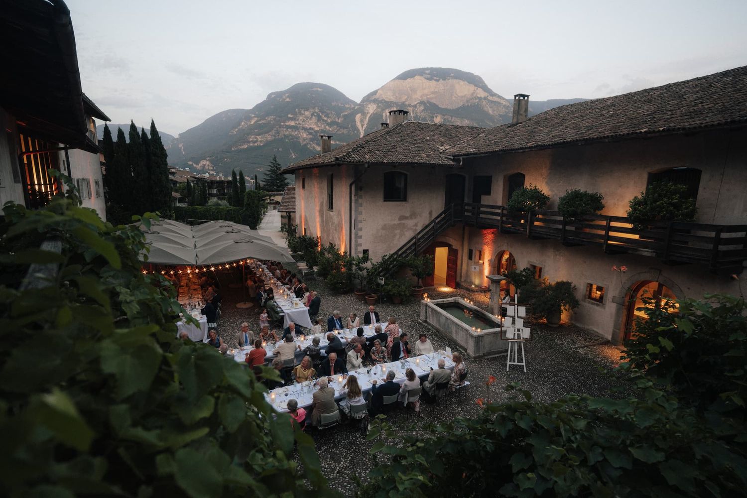 Outdoor wedding reception at dusk in an Italian villa courtyard with mountain backdrop and string lights.