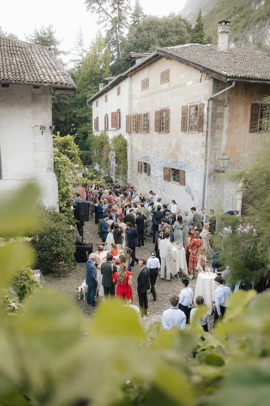 Elegant outdoor wedding reception at a rustic Italian villa with guests mingling in a courtyard surrounded by lush greenery.