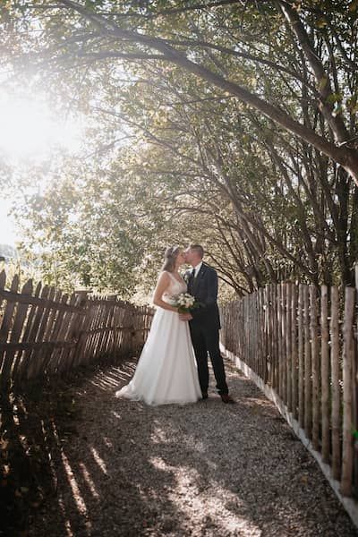Brautpaar küsst sich, sie stehen auf einem kleinen Weg mit Holzzaun. Hochzeitsfotograf Krems, Wachau und Wien