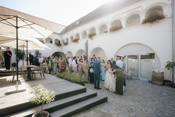 Elegant wedding reception in a historic courtyard with arched architecture, guests mingling outdoors on a sunny day.