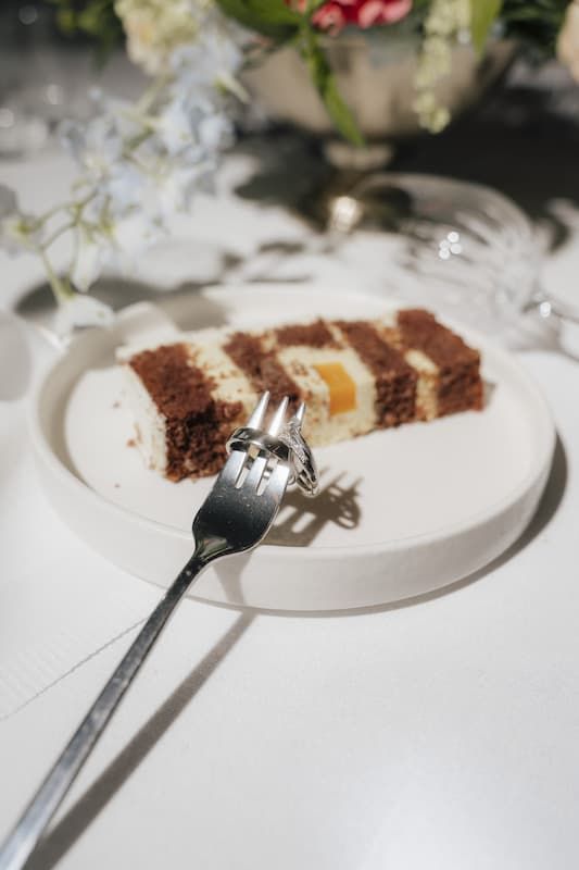 A slice of chocolate and cream layered cake on a white plate with a silver fork at a wedding reception.