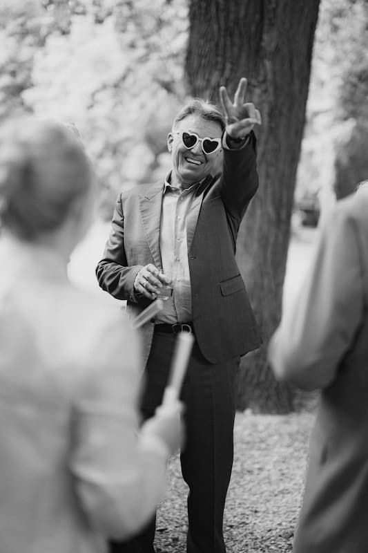 Man in heart-shaped sunglasses waving outdoors in black and white wedding photo.