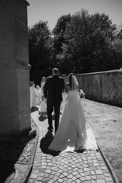 Black and white photo of bride and groom walking on cobblestone path after wedding ceremony.