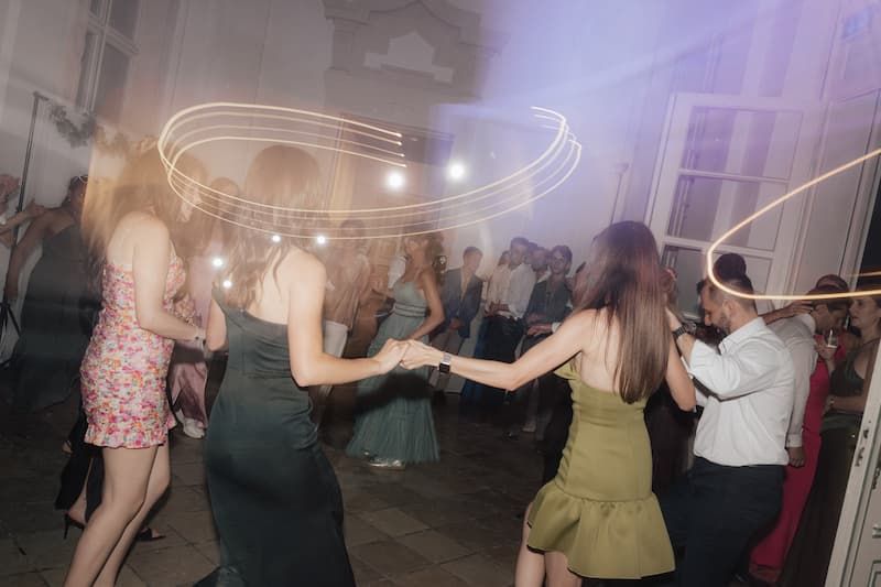 Guests dance energetically with light trails at a lively wedding reception party.