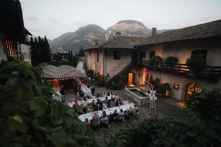 Elegant outdoor wedding reception in a rustic Italian courtyard with mountain views at dusk.