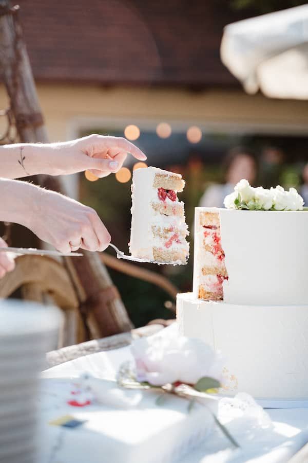 Hochzeitsfotografie in Niederösterreich: weißes Hochzeitstortenstück mit Himbeeren wird mit einer Kuchengabel herausgehoben