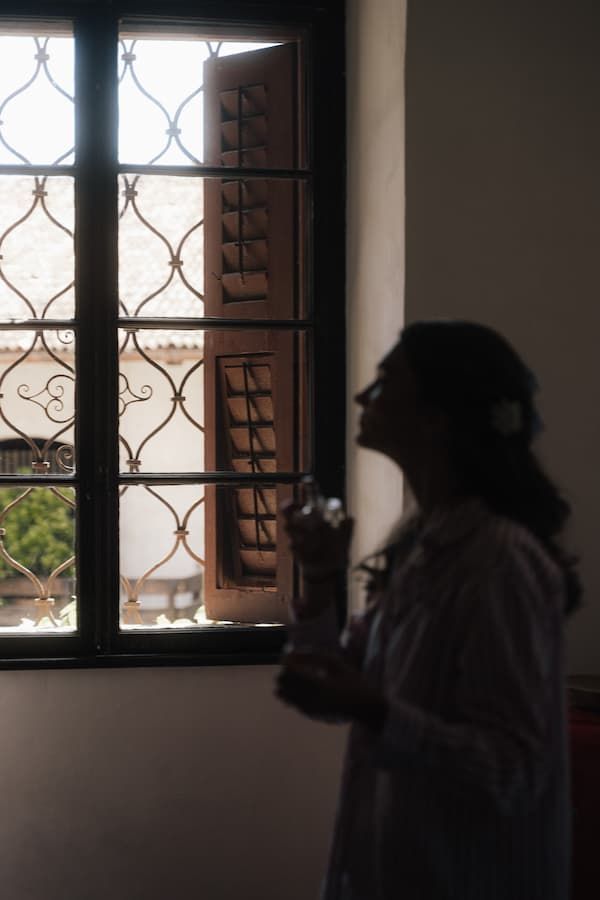 Silhouette of a woman holding a camera near an ornate window with wooden shutters and decorative iron grilles.