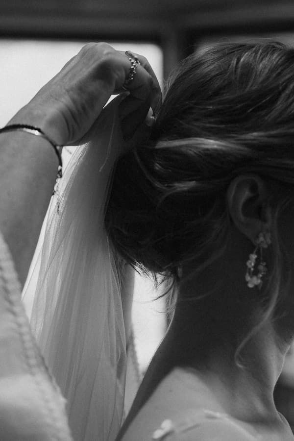 Black and white photo of a bride having her veil pinned into an elegant updo hairstyle.
