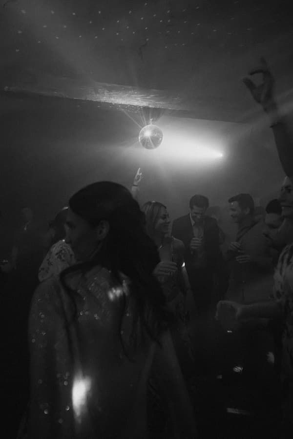 Black and white photo of people dancing at a nightclub with a disco ball glowing overhead.