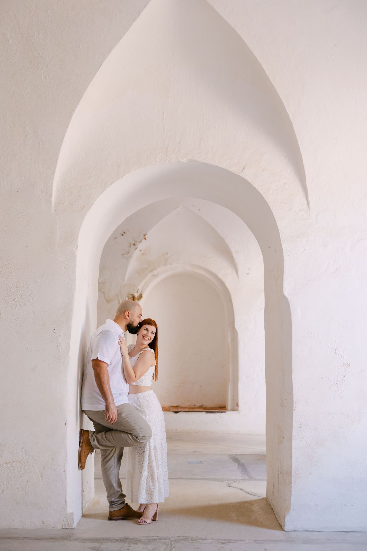 Two figures dance gracefully under white arched hallway in minimalist architectural setting.