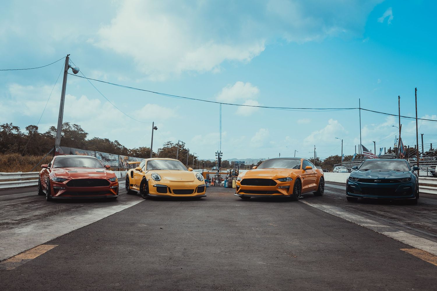 Four colorful sports cars lined up on a road under blue sky.