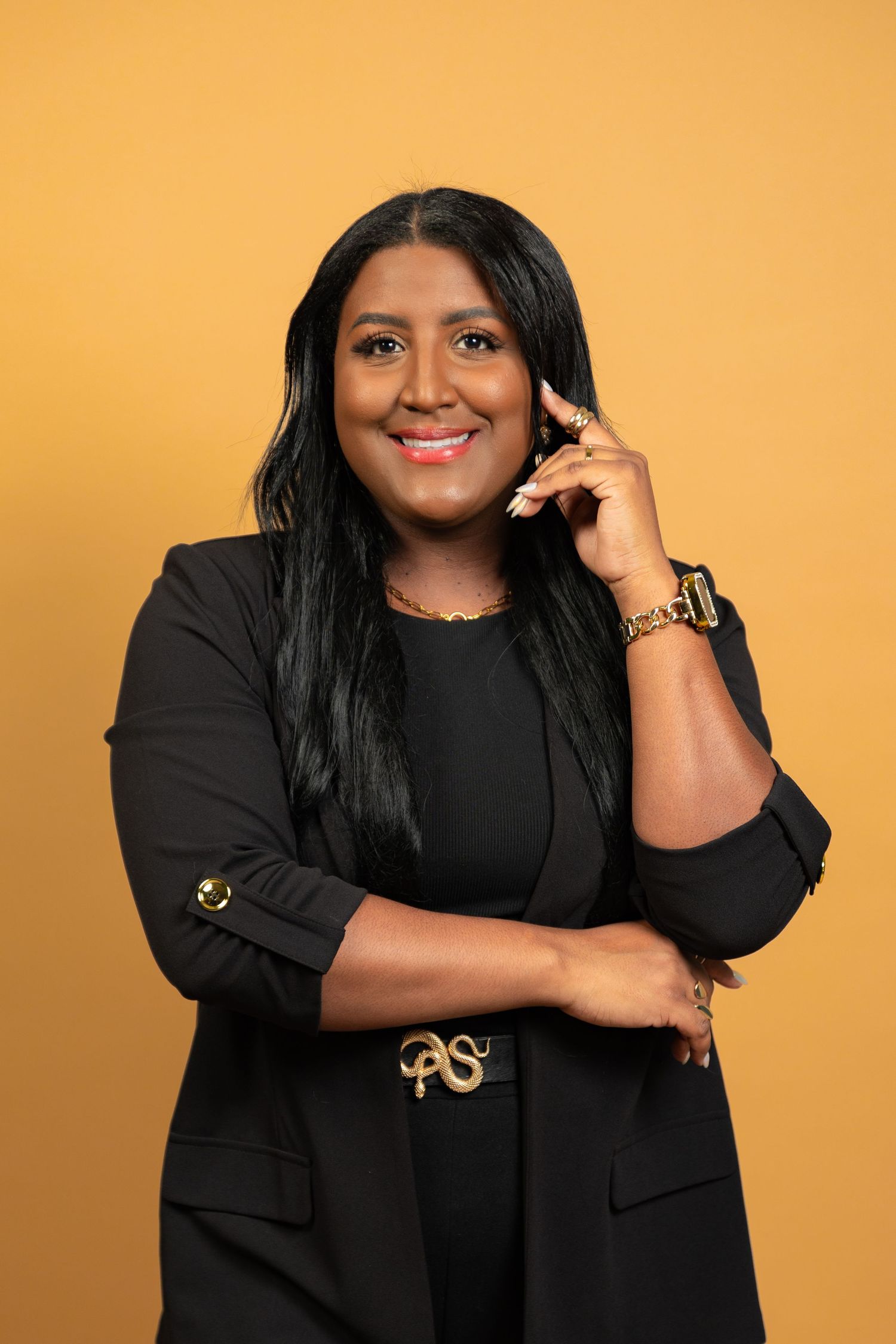Professional portrait against orange background showing someone in black business attire with a bright smile while on phone call.