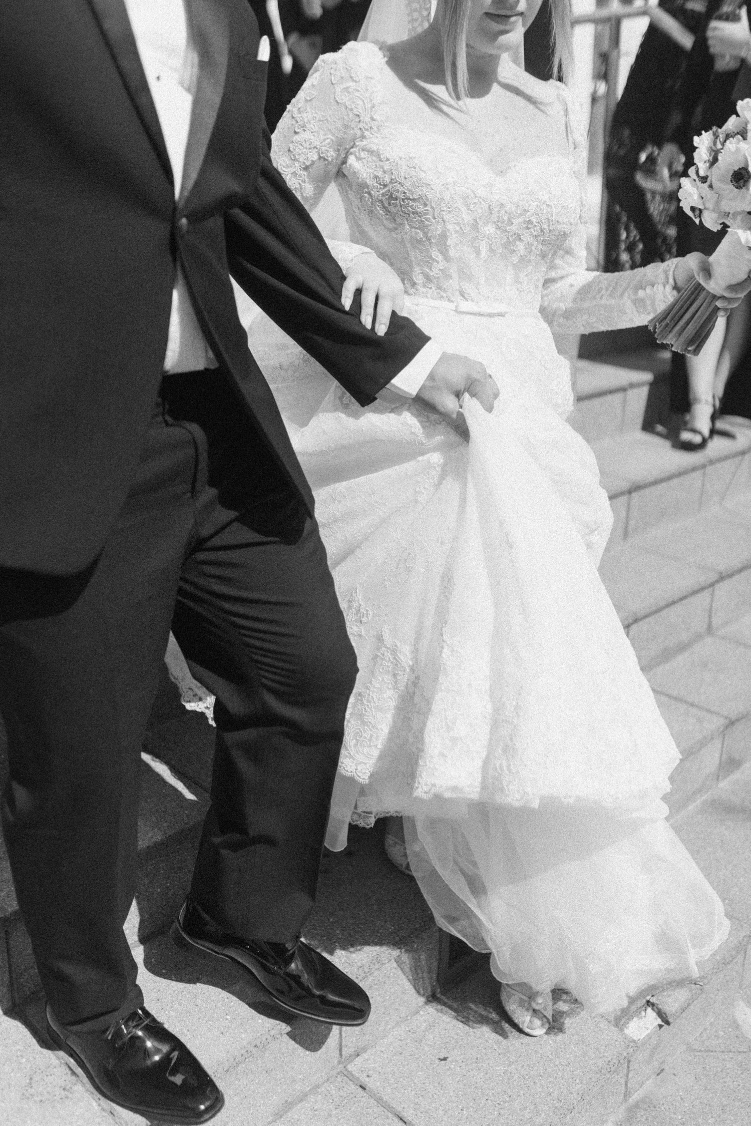 Black and white wedding photo showing bride's lace dress and groom's formal suit as they stand together outdoors.