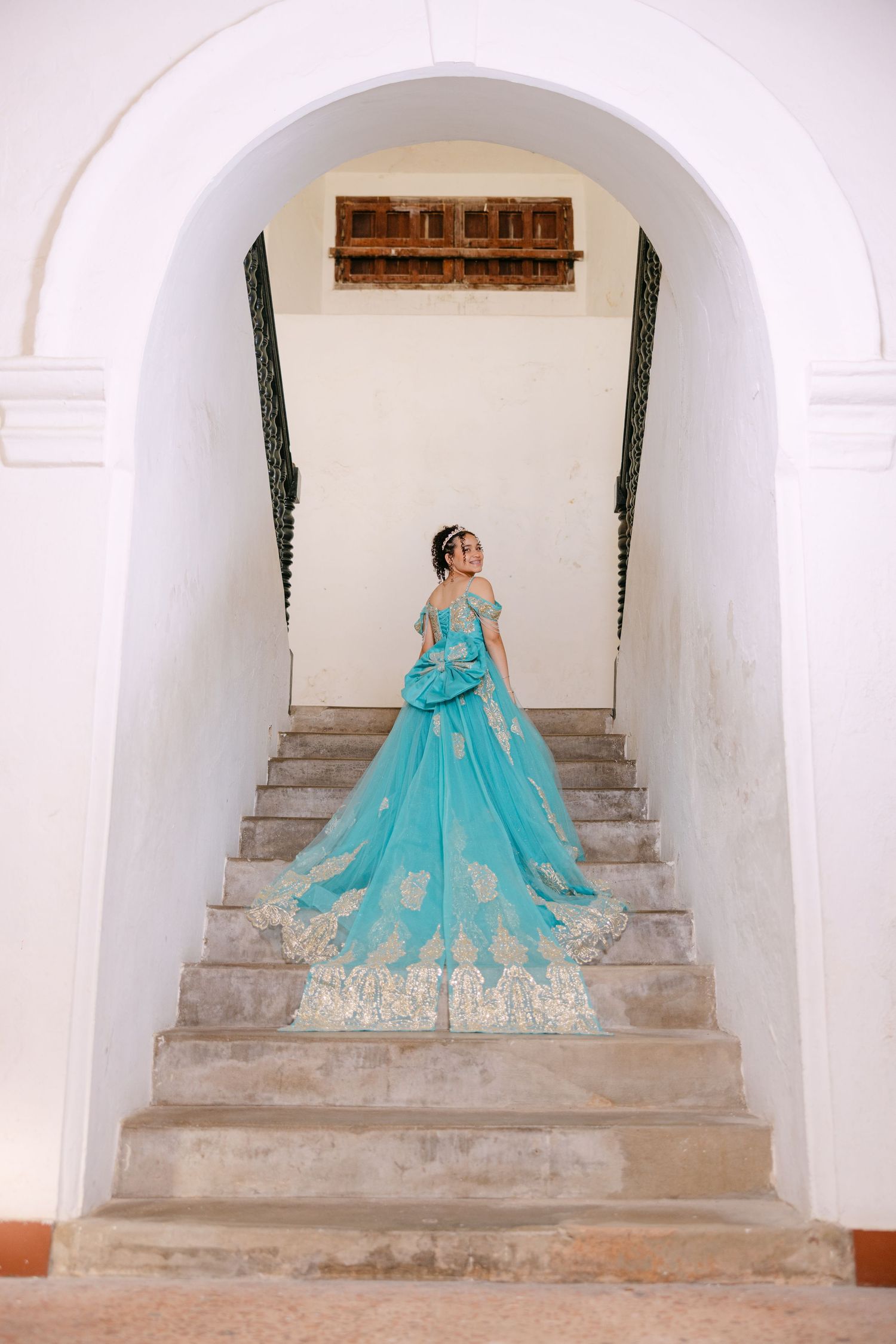 A turquoise ball gown with lace details photographed in sequence on stone steps under white archways.