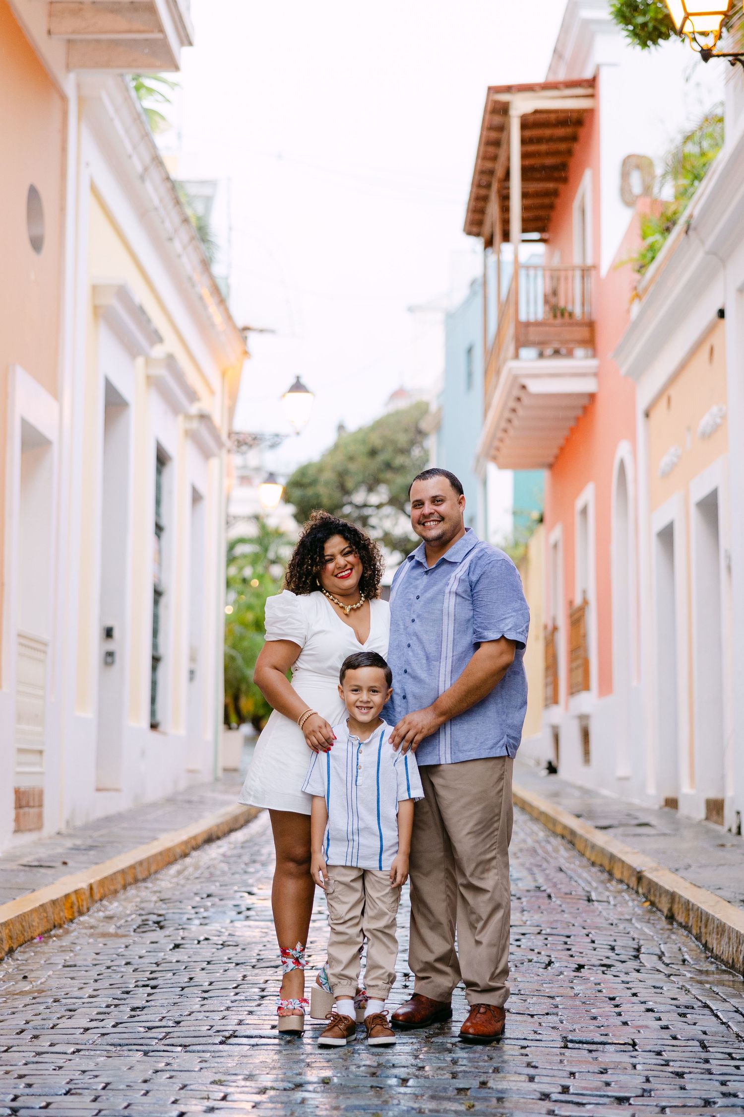 A family shares joyful moments together on a charming cobblestone street lined with colorful colonial buildings.