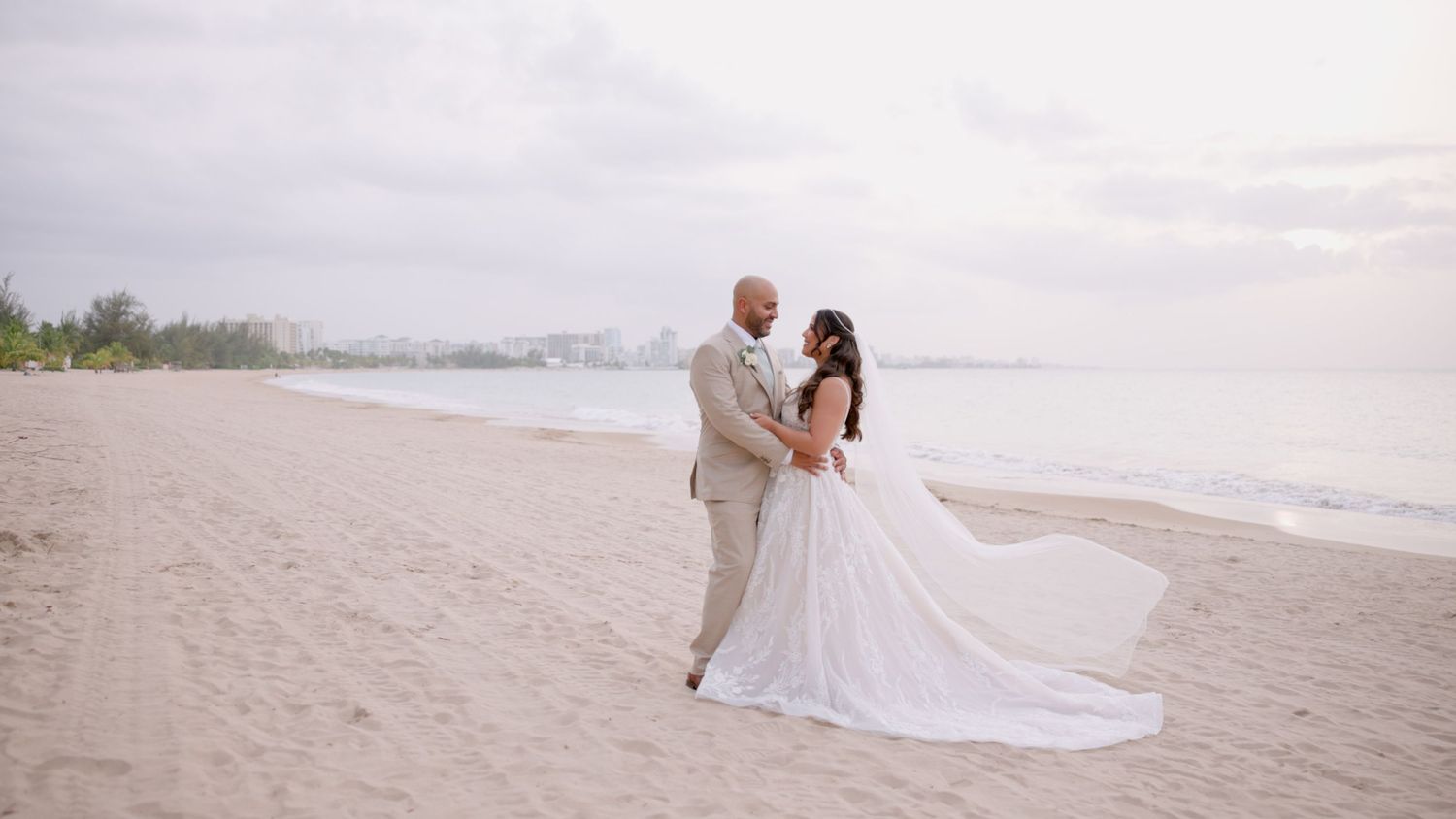 Wedding couple embracing on beach with flowing white dress.