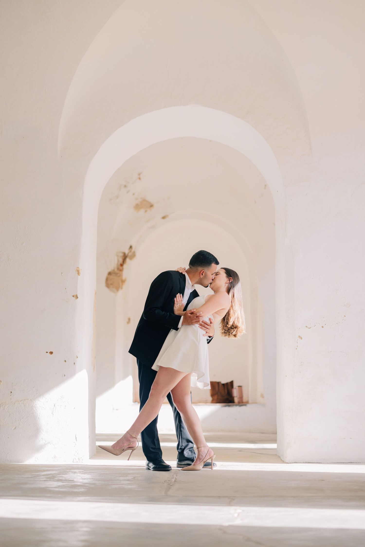 A romantic dance pose captured in a sunlit white archway.